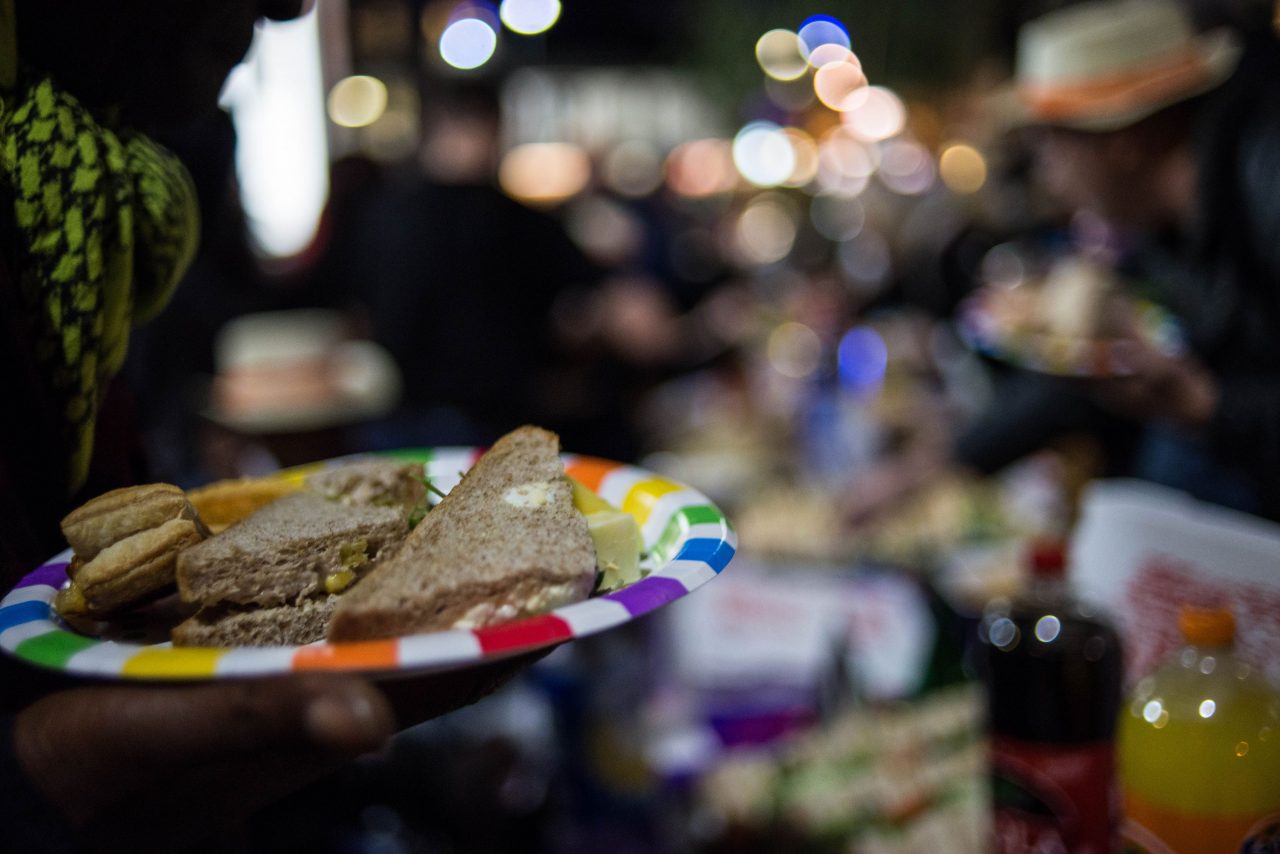 A close shot of sandwiches and sausage rolls on a brightly coloured paper plate at the launch of the public realm arts project, As You Change, So Do I.